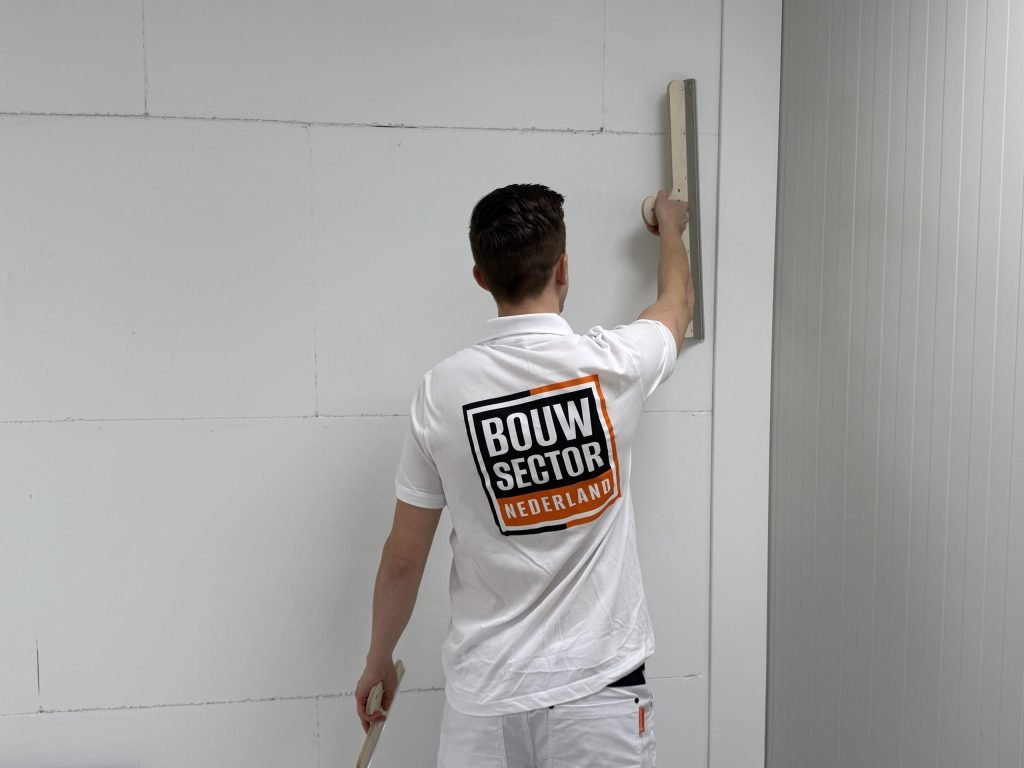 Stukadoor met het logo van Bouwsector Nederland op zijn rug strijkt een muur glad met een lange spaan
