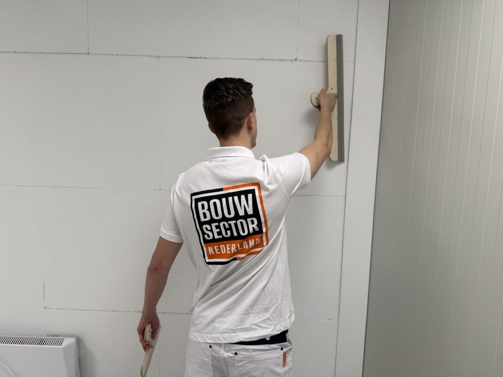Stukadoor van Bouwsector Nederland houdt een spaan hoog tegen de wand om een naad weg te werken