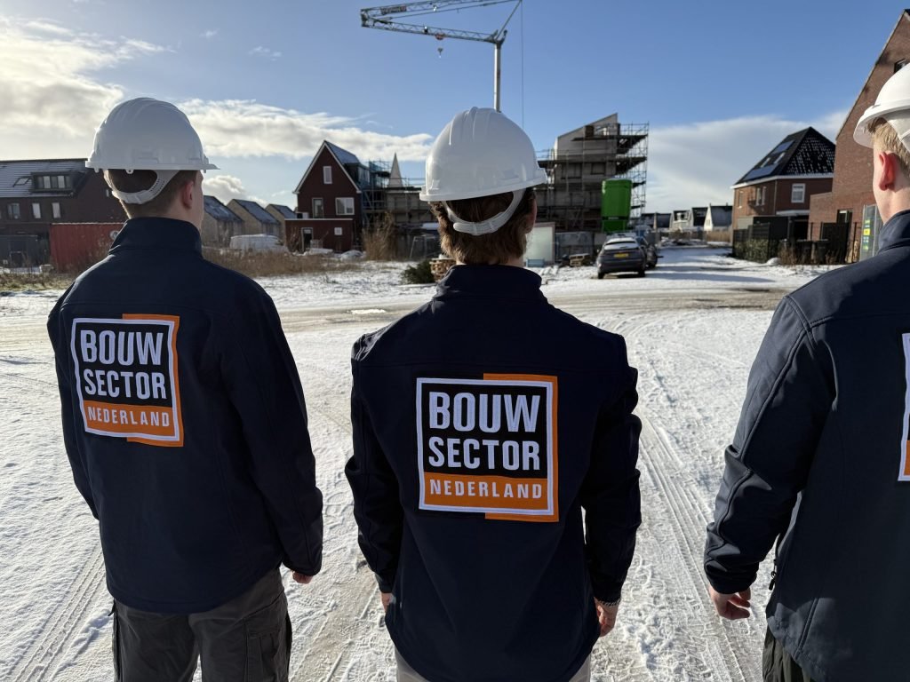 Drie vakmensen in bedrijfsjas van Bouwsector Nederland kijken samen naar een woning in aanbouw
