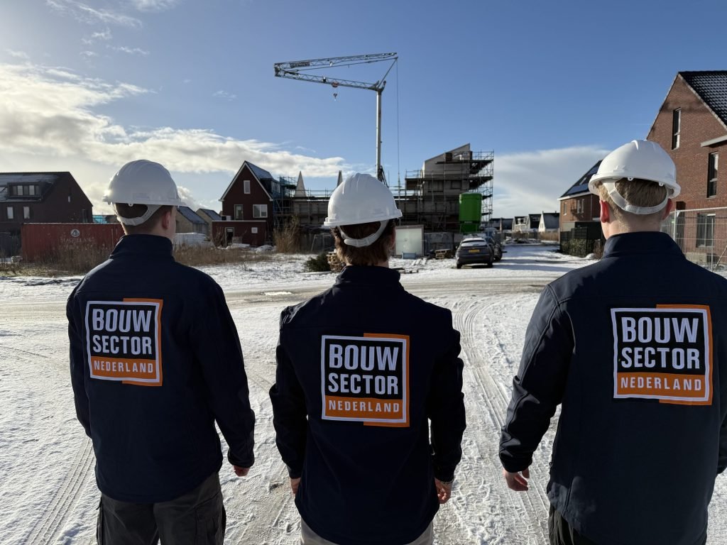Drie medewerkers van Bouwsector Nederland met witte helm kijken naar een nieuwbouwwijk in aanbouw